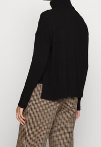 Svart polotröja med ribbad textur, neddragna axlar och avslappnad passform. Matchad med mönstrade bruna och svarta byxor.