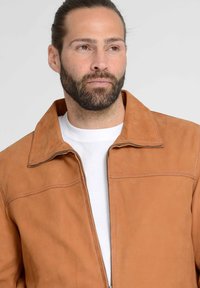Braune Lederjacke mit einem ausgeprägten Kragen, Reißverschluss und geraden Nähten. Getragen über einem weißen T-Shirt mit einer glatten Textur.