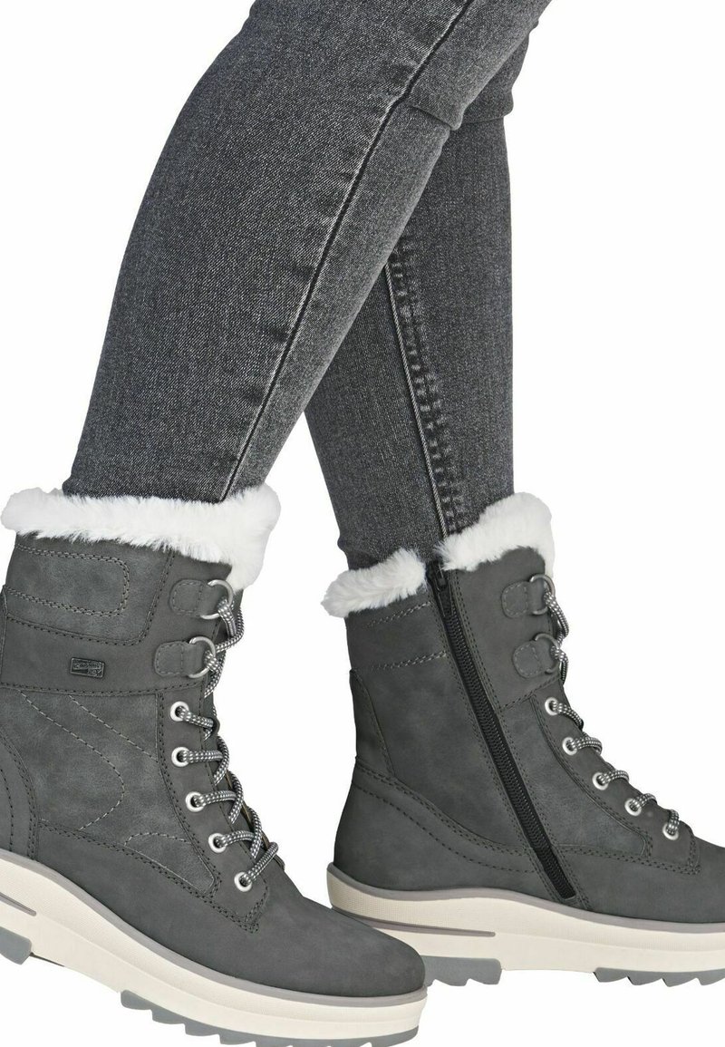 Graue Wildleder-Stiefeletten mit einem weißen Kunstfellbund, Schnürdesign, seitlichem Reißverschluss und einer groben, strukturierten Gummisohle.