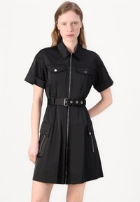 Vestido preto de manga curta feito de material leve, apresentando um fecho de correr frontal, dois bolsos no peito e uma cintura com cinto com acessórios em prata.
