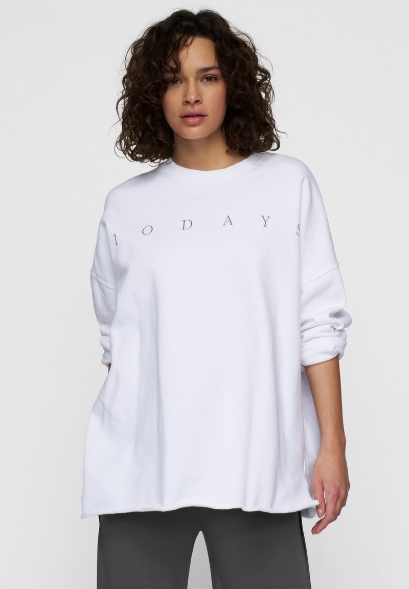 Sudadera oversized blanca con mangas enrolladas que presenta el texto gráfico "1 0 D A Y S" en gris. Material suave y un corte relajado, con un escote redondeado.