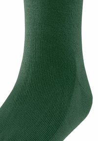 Calzino verde scuro con un pattern ribattuto testurizzato, che mostra l'area della caviglia e del piede, enfatizzando il suo materiale morbido e la vestibilità aderente.