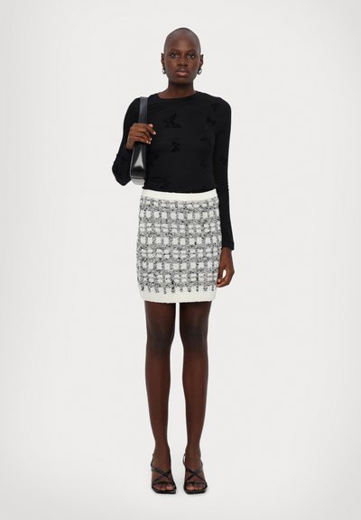 Black long-sleeve top with butterfly pattern, paired with a textured white and black checkered skirt, complemented by strappy black heels.