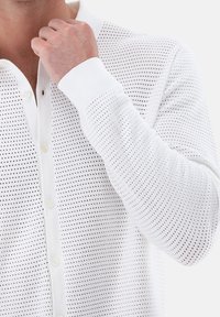 Biała koszula z długim rękawem wykonana z lekkiego, teksturowanego materiału z perforowanym wzorem i zapięciem na guziki.