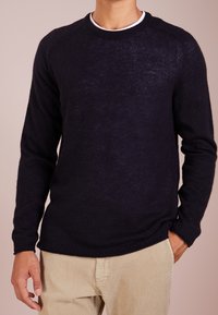 Marineblauer Rundhalspullover aus weichem Material, mit langen Ärmeln und gerippten Säumen, kombiniert mit beigen corduroyhosen.