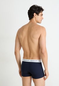 Marineblaue Baumwollshorts mit einem weißen markierten Bund, der eine enge Passform und glatte Textur bietet, von hinten gezeigt.
