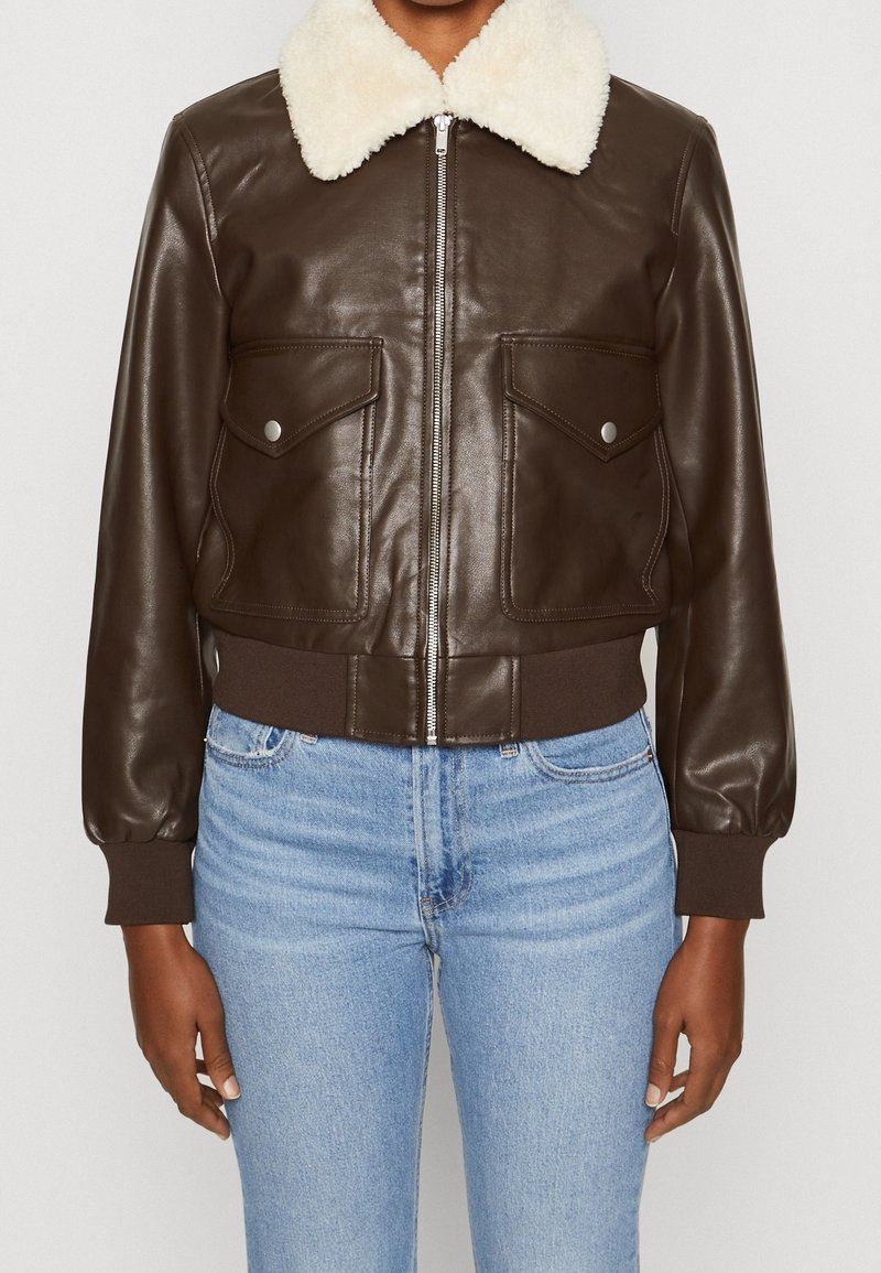 Giacca bomber in pelle marrone con colletto in finta shearling crema, orlo a coste, due tasche sul petto, chiusura a zip e maniche a palloncino.