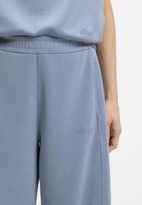 Light blue sweatpants in soft fabric with an elastic waistband, featuring side pockets and subtle embroidered logo detail.