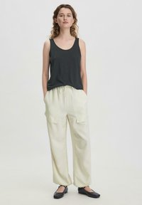 Donkergrijze mouwloze tanktop gecombineerd met lichtbeige wijde broek met zijzakken, een gestrikte tailleband en platte zwarte schoenen.