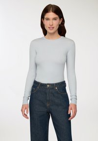 Maglia azzurro chiaro a maniche lunghe con scollatura rotonda e silhouette aderente, abbinata a jeans blu scuro a vita alta con chiusura a bottone.