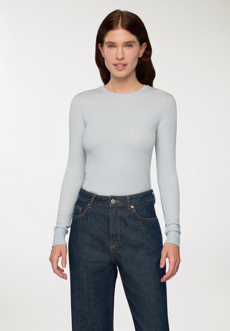 Maglia azzurro chiaro a maniche lunghe con scollatura rotonda e silhouette aderente, abbinata a jeans blu scuro a vita alta con chiusura a bottone.
