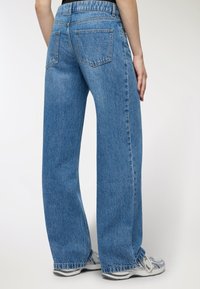 Szerokie niebieskie dżinsy wykonane z denimu, z tylkimi kieszeniami i lekko spranym wykończeniem. Dolna część nogawek jest luźna i niestrukturalna.