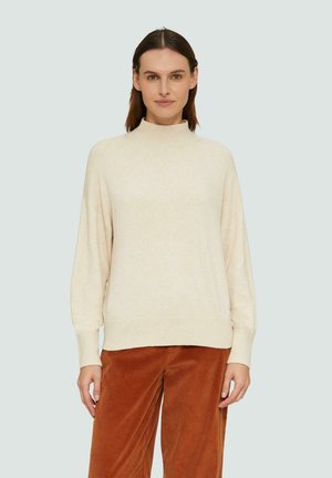Beige hoge halstrui met lange mouwen, zachte textuur en geribbelde zoom, gecombineerd met roestkleurige ribfluweel broek.