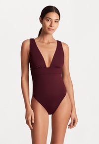 Maiô de uma peça cor bordô com decote em V profundo, alças largas e detalhes franzidos na cintura. Tecido liso e elástico.