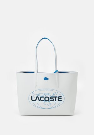 Valkoinen Lacoste-kangaskassi sinisellä sisäpuolella, sinisellä krokotiililogolla ja sinisellä maailmankarttakuviolla, jossa on etuosassa teksti "LACOSTE".