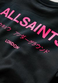 Čierna mikina s odvážnym ružovým textom, obsahujúca "ALLSAINTS LONDON" a ďalšie znaky v rôznych jazykoch, hladká textúra látky.