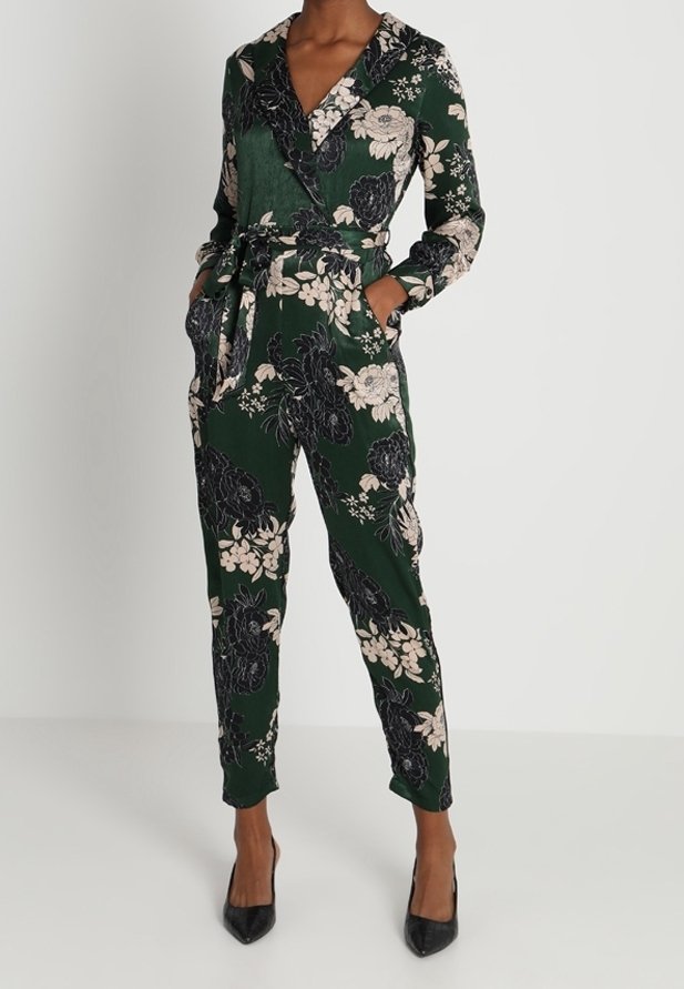 Combinaison portefeuille à manches longues à fleurs vertes, avec ceinture à la taille, poches latérales, et escarpins noirs à bouts pointus.