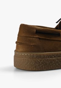Brune svinesneaker med rund ryg, tekstureret gummisål og kontrastsyninger langs kanten. Snørebånd trukket gennem huller.