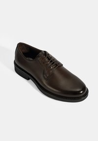 Bruine leren derby schoen met een gladde afwerking, afgeronde neus, vetersluiting aan de voorkant en een lage zwarte zool; heeft minimale stikdetails.