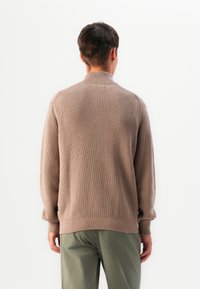 Hellbraunes, gestricktes Sweatshirt mit einem gerippten Design, hohem Kragen und langen Ärmeln. Verfügt über einen strukturierten Stoff und eine lässige Passform.