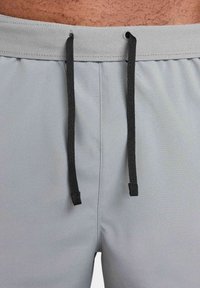 Grå idrottsshorts med ett slätt, lättviktigt tyg, med svarta dragsnören och sydd midja. Inga synliga mönster eller logotyper.