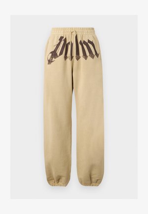 Bézs színű melegítőnadrág elasztikus derékpánttal, húzózsinórral, oldalzsebekkel, rugalmas mandzsettákkal és fekete gótikus stílusú felirattal az elülső derékrészen.