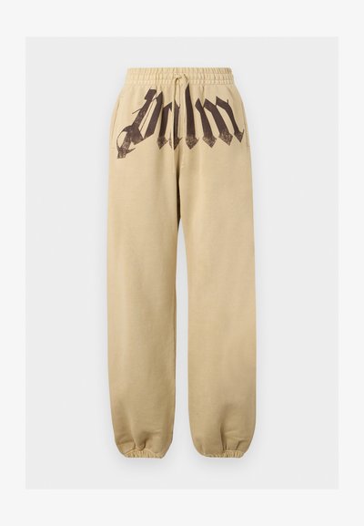 Μπεζ φόρμες με ελαστική μέση, κορδόνι, πλαϊνές τσέπες, ελαστικές μανσέτες και μαύρο γοτθικό κείμενο στην μπροστινή μέση.