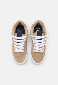 Adidași din suede bej cu șireturi albe, un accent bleumarin pe limbă, superior texturat și o talpă din cauciuc albă. Proiectați pentru uz casual.