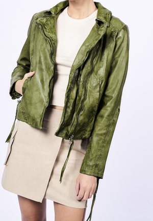 Groene leren motorjack met een cropped ontwerp, gestructureerde afwerking, ritsluiting en trekkoordaccenten. Draagt over een beige top en rok.
