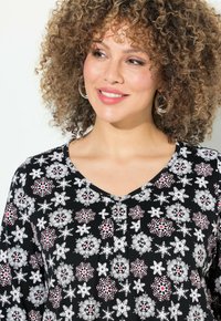 Blouse noire avec un col en V et un motif de flocons de neige floraux en blanc et rouge, avec une texture douce et une coupe décontractée.