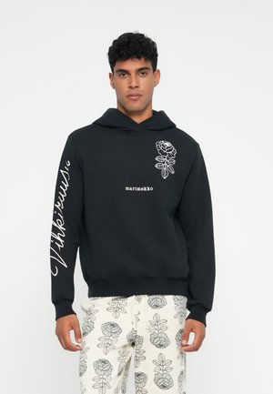 Sweatshirt à capuche noir avec impression florale blanche sur la poitrine gauche et la manche, comportant le texte "marimekko". Détails : poignets et ourlet côtelés.