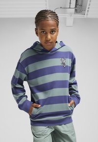 Hoodie s zelenim i mornarskim prugama, izrađen od mekanog materijala. Ima izvezeni dizajn na lijevoj strani prsnog koša i prednju džep.