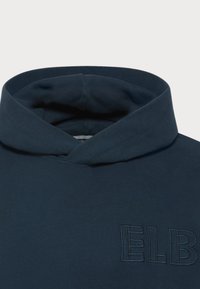Námořnická modrá mikina s vysokým límcem, se vyšitým logem "ELB". Vyrobena z měkké tkaniny, má hladký povrch a strukturovaný design.