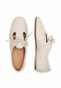 Ballerine in pelle crema con dettagli a intaglio, punta arrotondata e accentuazione a fiocco. Presentano una texture liscia e una suola bassa e flessibile.