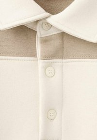 Polo avec un design bicolore crème et beige, doté d'un col à revers, de trois boutons et d'un tissu doux et texturé.