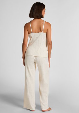 Roomkleurige mouwloze top en broek met wijde pijpen van gestructureerde stof, met kleine roze accenten en een kanten rand langs de halslijn.