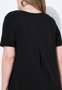 Top nero a maniche corte con scollatura rotonda, caratterizzato da una delicata piega sul retro e da un tessuto liscio e strutturato. Design minimalista.