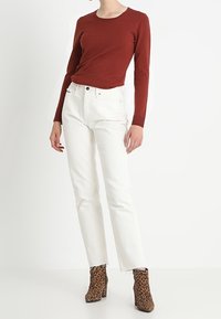 Rostfarbener Langarm-Oberteil kombiniert mit weißen, geraden Jeans und braunen, leopardenmusterierten, hohen Stiefeletten; klassisches Design mit glatter Textur.