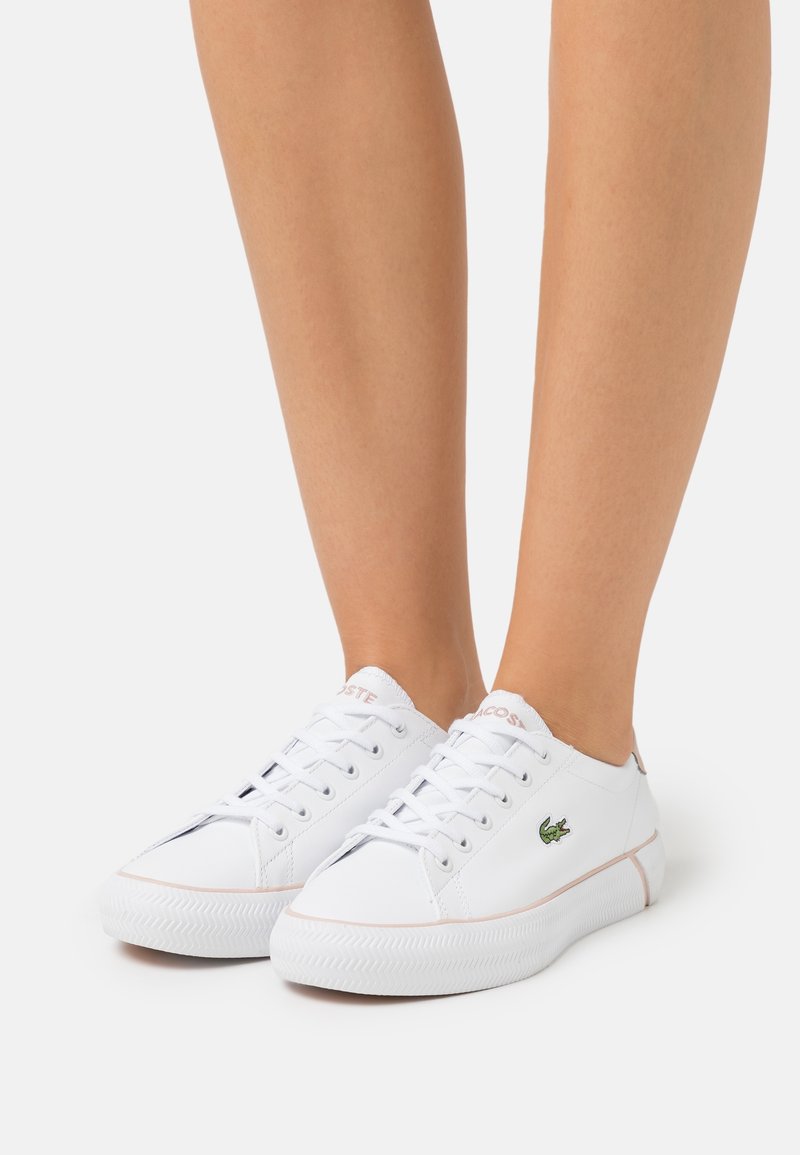 Sneaker bianche con lacci, dotate di una tomaia in pelle liscia, accenti rosa a contrasto e un logo ricamato verde sul lato. Suola in gomma testurizzata.