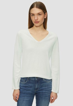 Lichtgroene longsleeve top met een V-hals. Gemaakt van zachte stof, met een ontspannen pasvorm en een gladde textuur. Gecombineerd met blauwe jeans.