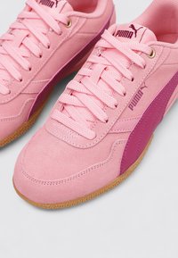 Zapatillas de ante rosa con puntera redondeada, sistema de cordones clásico y una franja lateral en un tono de rosa más oscuro. Suela de goma con agarre texturizado. Logotipo de Puma destacado.