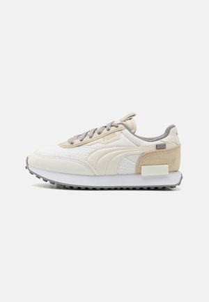 Sneaker bianca e beige realizzata in materiali mesh e suede, con lacci grigi e un distintivo accento testurizzato sul tallone. Design a profilo basso.