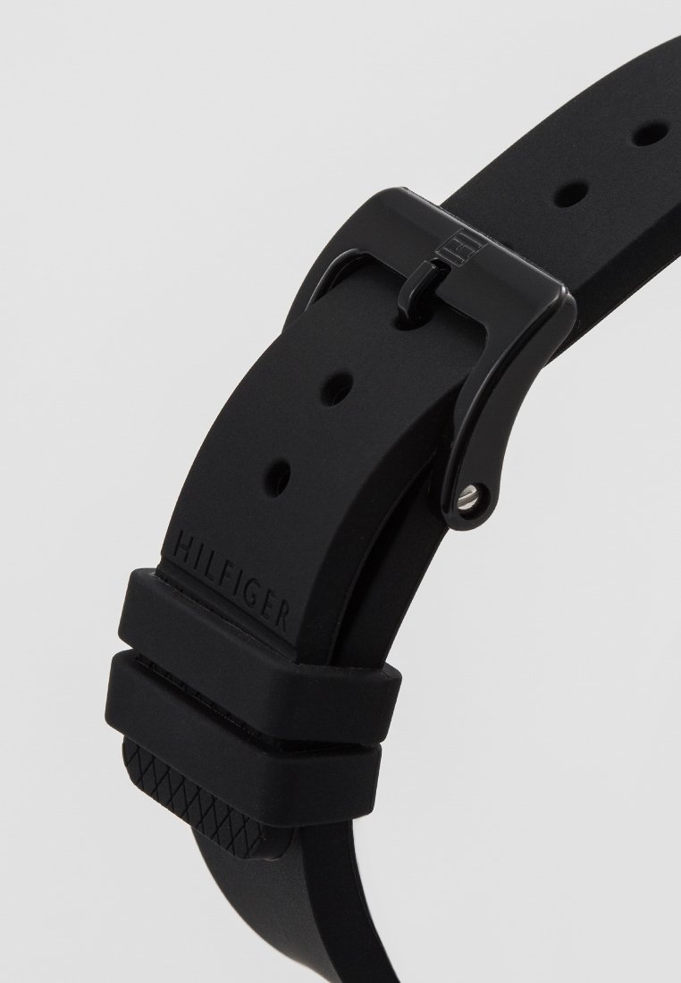Czarny silikonowy pasek do zegarka z wieloma otworami, czarna metalowa klamra i wytłoczone na końcu paska "Hilfiger".