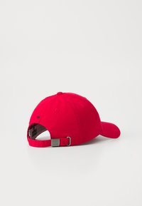 Casquette de baseball en coton rouge avec une visière incurvée, une sangle ajustable et une boucle en métal à l'arrière. Doublure texturée visible à l'intérieur.
