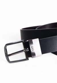 Cinturón de cuero negro con hebilla metálica plateada. La hebilla tiene una forma rectangular y un acabado cepillado, creando una apariencia elegante.