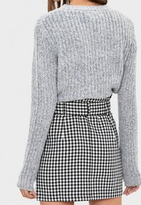 Šedý žebrovaný pletený svetr s dlouhými rukávy, který je kombinován s černo-bílou kostkovanou mini sukni s vysokým pasem a sklady.
