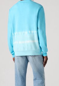 Sudadera azul claro con un efecto tie-dye degradado que se funde a blanco en la parte inferior. Presenta puños y dobladillo acanalados, textura de tela suave.