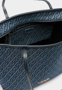 Borsa tote in tessuto blu navy con interno decorato, dettagli in pelle e chiusura con zip. Dettaglio del logo dorato sull'esterno.