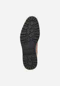 Semelle de chaussure en daim marron avec des crampons en caoutchouc noir profond présentant un motif floral pour l'adhérence, forme incurvée au niveau du talon.