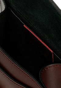 Bruine leren portemonnee met zwart interieur, voorzien van een rode accenttag en zichtbare stiksels, met een glad oppervlak en afgeronde randen.